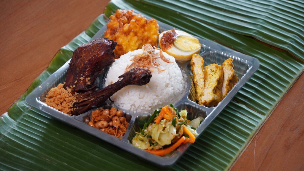 Nasi kotak DKBoga Catering Bali dengan ayam sisit bumbu Bali, telur sambal, urap, mie goreng, tahu tempe, perkedel, sambal geprek, kerupuk, dan air mineral